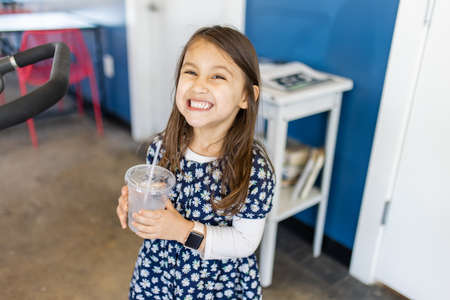 Adorable happy little girl holding a plastic cup in restaurantの写真素材