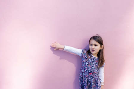Adorable distressed little girl wearing standing in front of a pink wallの写真素材