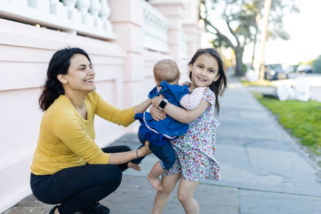 Happy adorable little girl carrying her baby sister in peaceful street