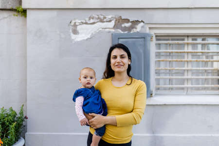 Beautiful happy mother holding her cute baby with gray wall as backgroundの写真素材