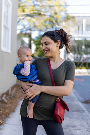 Happy mother holding her cute baby with blurry trees and houses as background