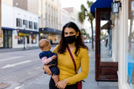 Mother wearing face mask and holding her cute baby in peaceful street