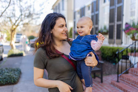 Beautiful happy mother holding her cute baby in peaceful neighborhoodの写真素材