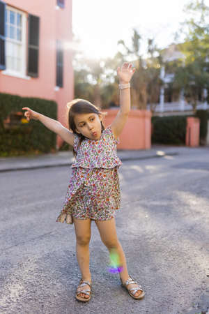 Happy little girl in flowered dress making funny pose in empty street
