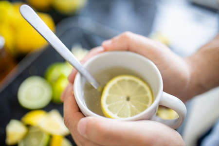 Male hands holding a cup of lemon tea above lime slicesの写真素材