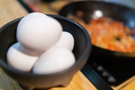 Eggs in small black bowl with blurry food in pan as backgroundの写真素材