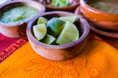Bowls of lime slices, green sauce, and lamb broth on colorful tableclothの写真素材