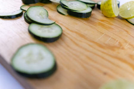 Fresh cucumber slices and a lime cut in half on wooden cutting boardの写真素材