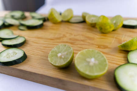 Fresh cucumber slices and halved limes on wooden cutting boardの写真素材