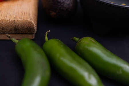 Green chili peppers next to a cutting board on black surfaceの写真素材