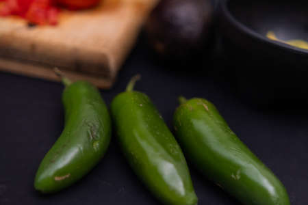 Green chili peppers next to a cutting board on black surfaceの写真素材