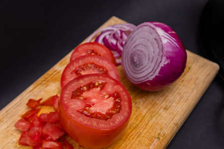 Sliced tomato and onion on cutting board above black surfaceの写真素材