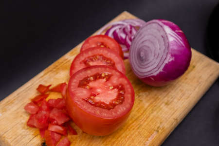 Sliced tomato and onion on cutting board above black surfaceの写真素材