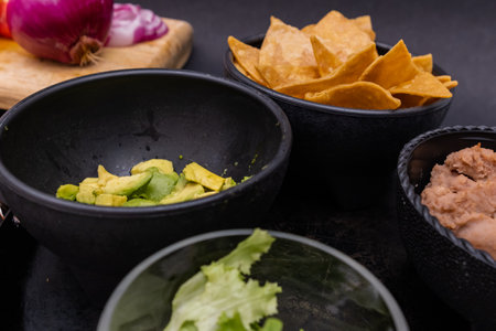Sliced vegetables and bowls of tortilla chips and beans with black backgroundの写真素材