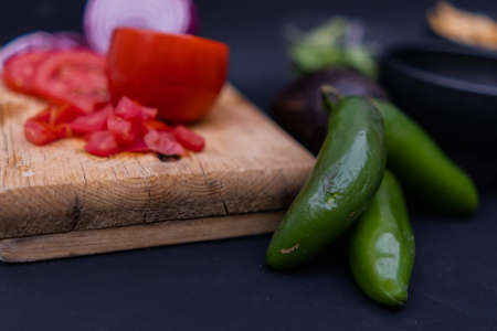 Sliced tomato and onion on wooden cutting board next to chili peppersの写真素材