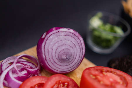 Sliced tomato and onion on cutting board with black and blurry backgroundの写真素材