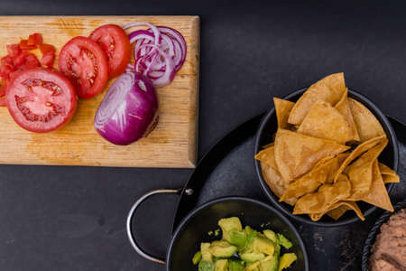 Sliced vegetables and bowls of tortilla chips and avocado on black surfaceの写真素材