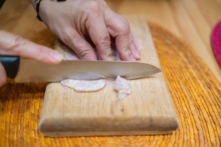 Hands chopping fresh turkey ham slices on a cutting boardの写真素材