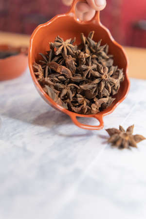 Hand holding clay pot of star anise seeds above white marble surfaceの写真素材