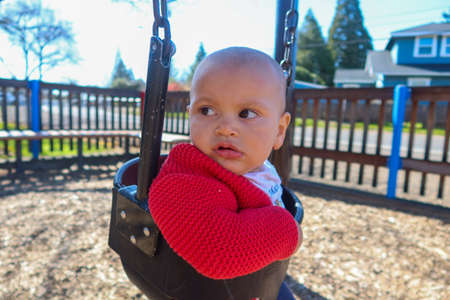 Adorable baby on swing with bright sky as backgroundの写真素材