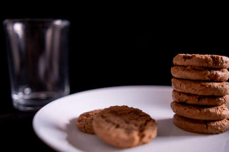 Stacked cookies on white plate and empty glass with black backgroundの写真素材