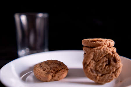 Stacked cookies on white plate and empty glass with black backgroundの写真素材