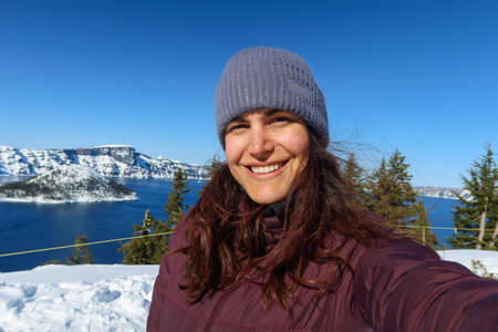 Happy woman taking selfie with beautiful snowy mountain range as background