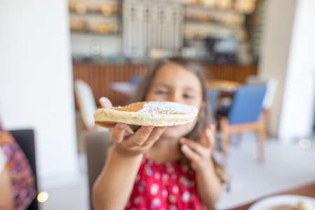 Cute little girl sitting at restaurant table and showing a pancakeの写真素材