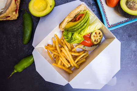 Tasty fries and sliced vegetables in white box above dark surface