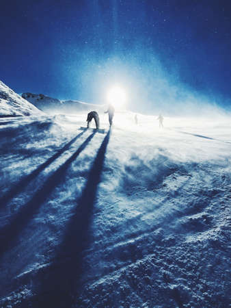 Silhouettes of snowboarders on a ski slope with a snowy sunの写真素材