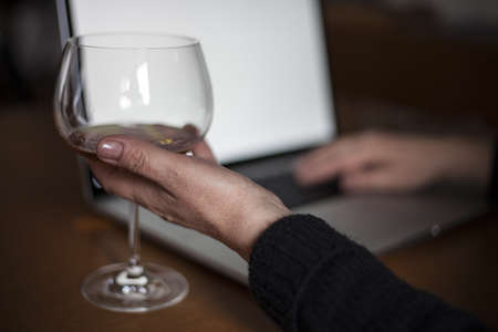 A middle aged woman drinking while working on her laptop