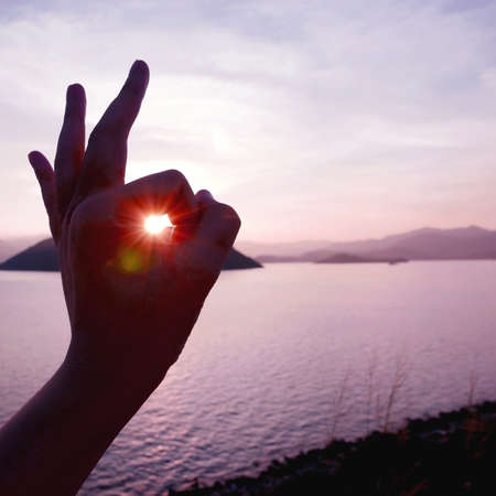 The sunlight is from human hand with mountain and the seaの写真素材