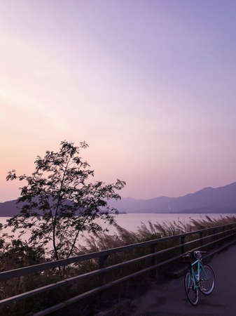 Mint green retro bicycle, road frame, mountain, lake and gradient sky at sunsetの写真素材