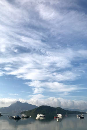 Vertical mountain, blue sky, yacht boats and cloudscape with reflection on the lakeの写真素材