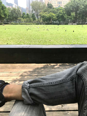 The vertical human leg, outdoor wooden floor and green field in city public parkの写真素材