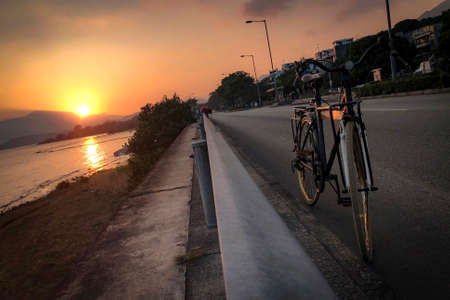 The silhouette of bicycle, fence, road and sea at sunsetの写真素材
