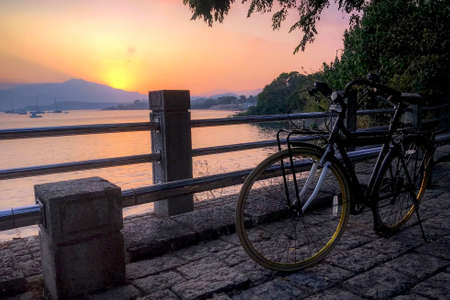 The silhouette of bicycle, fence and ocean at sunsetの写真素材