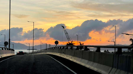 The horizontal landscape photograph mountain, car, road, fence, cloud and ocean at sunset