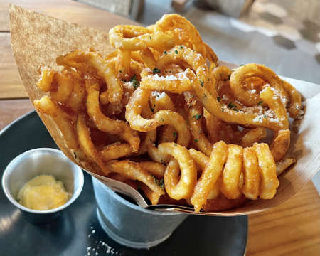 The horizontal crispy curly French fries inside silver bucket with sauce at cafe