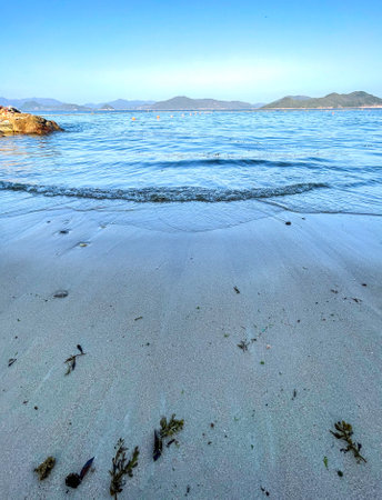 The outdoor beach, water waves, natural stones, blue sky and mountainsの写真素材