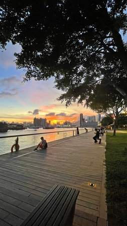 The vertical silhouette of people, park, building, boats on bay water at sunsetの写真素材