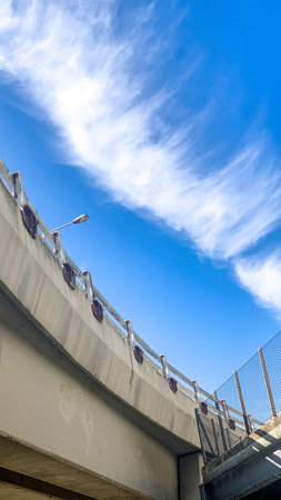 The bright blue sky and wispy clouds contrast with the concrete structure of the bridge, creating an...