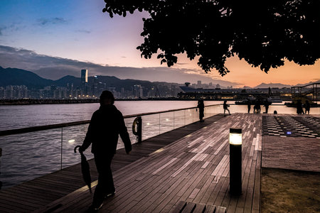 Silhouette of a person walking on a waterfront boardwalk at dusk in Hong Kongの写真素材