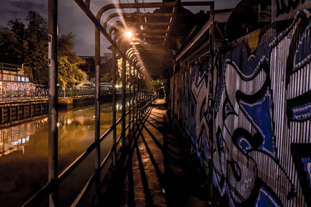 Urban night scene with graffiti art along a canal walkway, illuminated by streetlightsの写真素材