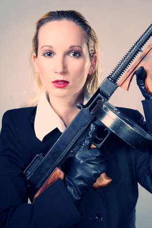 Mafia style fashion studio portrait - nice young woman posing with \\\"Tommy\\\" gun for figure and portrait photos in retro criminal style.の写真素材