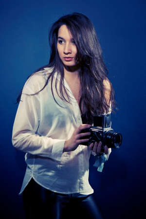 Cross-breed long hair Euro/Asian brunette girl posing like a photographer with classic camera in studio.の写真素材