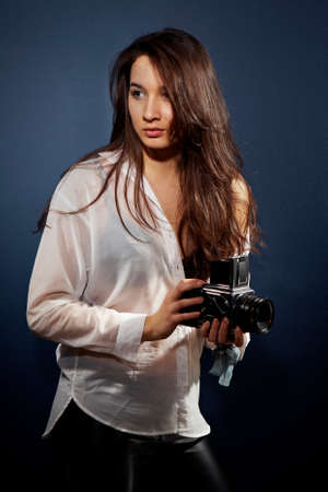 Cross-breed long hair Euro/Asian brunette girl posing like a photographer with classic camera in studio.の写真素材