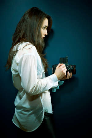 Cross-breed long hair Euro/Asian brunette girl posing like a photographer with classic camera in studio.の写真素材