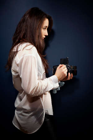Cross-breed long hair Euro/Asian brunette girl posing like a photographer with classic camera in studio.の写真素材