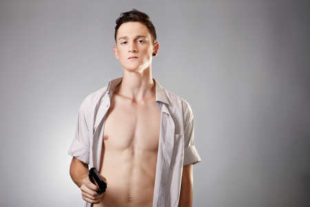 Young man with shaped body posing in studio with handgun for \"like criminal\" portraits.の写真素材